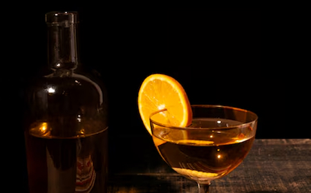 Бутылка красного вина, бокал с вином и штопор с пробкой на тёмной поверхности